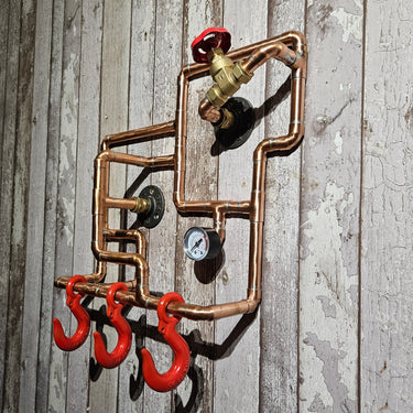 Steampunk wall rack with copper pipes, pressure gauge, and red industrial hooks on wood panel
