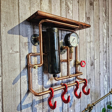 Industrial steampunk wall shelf with copper pipes, pressure gauge, and red hooks on wood panel