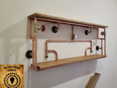 Industrial steampunk wall shelf with copper pipes, wood shelves, red valve handles, and gauge.