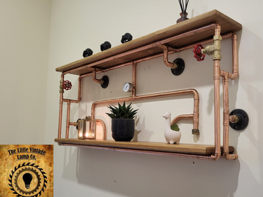 Industrial steampunk pipe wall shelf with wooden planks, copper pipes, and vintage decor accents.