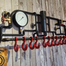 Handmade steampunk industrial coat rack with red hooks, gauge, and pipework on rustic wood wall