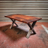 Industrial steampunk coffee table with wooden top and metal X-frame legs on red floor
