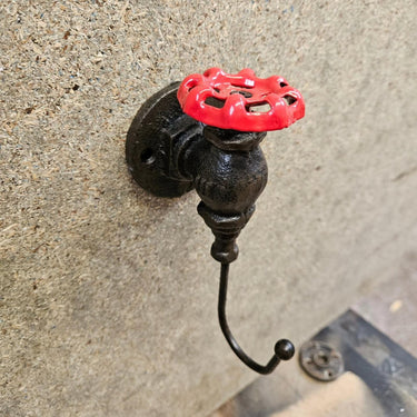 Industrial steampunk wall hook with red valve handle mounted on a textured wall