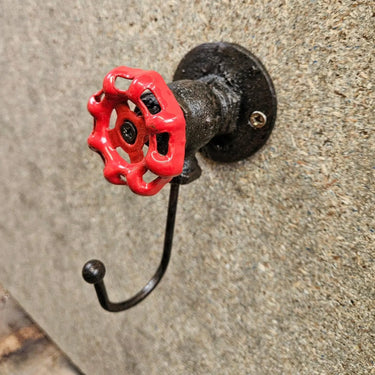 Industrial wall hook with red valve handle, steampunk pipe decor on textured wall.