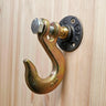 Industrial steampunk coat hook with metal flange mounted on light wood wall.