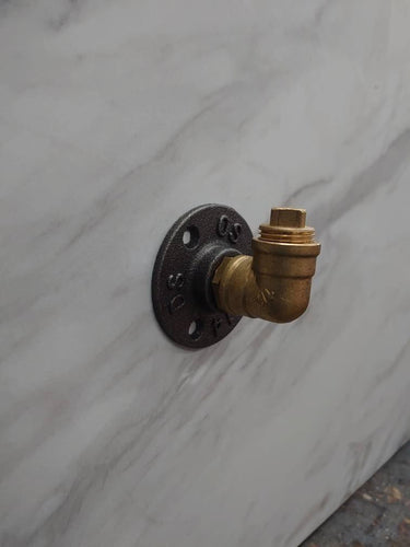 Brass industrial coat hook with a pipe fitting design on a marble wall