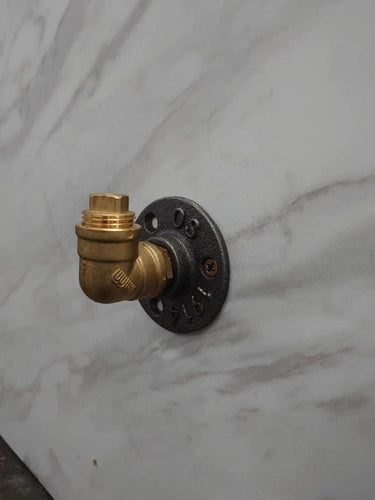 Industrial brass coat hook with black flange mounted on marble wall