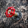 Industrial coat hook with red valve handle, mounted on metal flange against stone wall