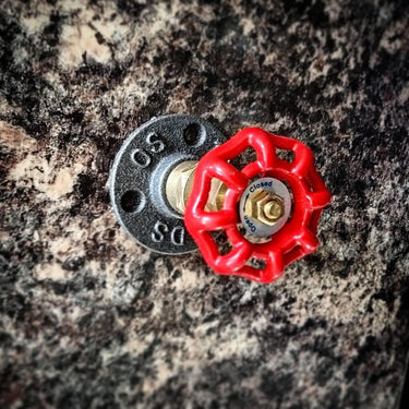 Industrial wall coat hook with red valve handle on textured surface