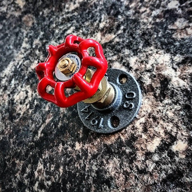 Industrial coat hook with red valve handle mounted on a stone wall