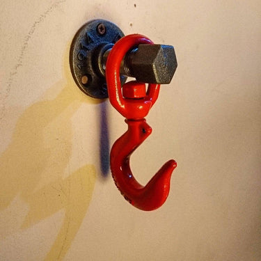 Industrial wall-mounted coat hook with red metal hook and black flange on a light wall