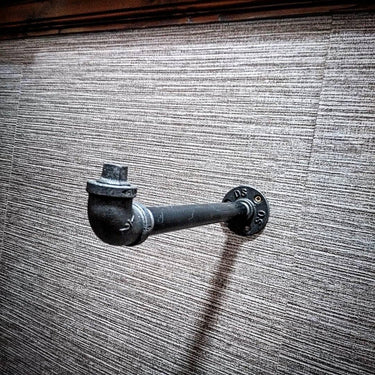 Wall-mounted industrial pipe clothes hanger rail against textured wall