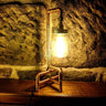 Industrial pipe style table lamp with mason jar shade on wooden surface against stone wall