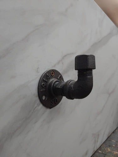 Industrial rustic coat hook made from black iron pipe against marble wall