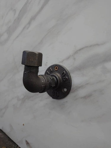 Industrial rustic coat hook made from metal pipe mounted on a marble-effect wall.