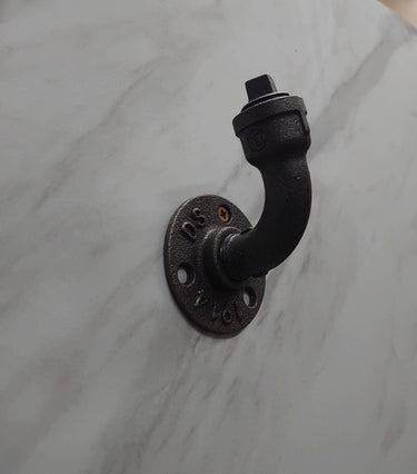 Industrial steampunk coat hook made from black iron pipe on a marble wall