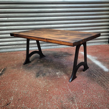 Industrial steampunk coffee table with dark wood top and black cast iron legs on concrete