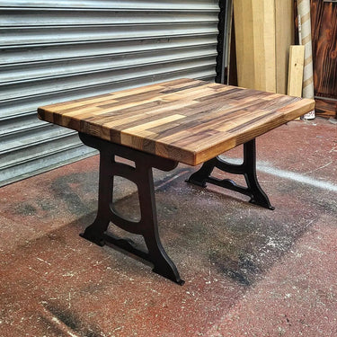 Industrial steampunk coffee table with iron legs and reclaimed wood top on workshop floor