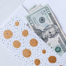 US twenty dollar bills in a white and gold polka dot envelope on a white surface