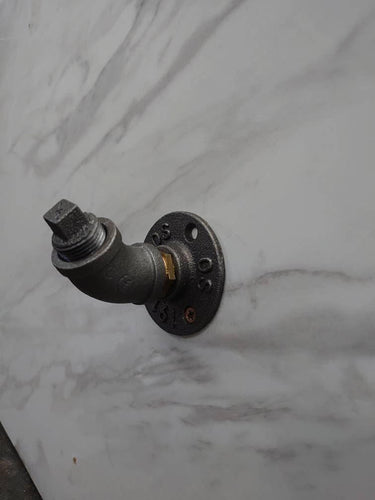 Retro industrial pipe coat hook mounted on a marble-effect wall
