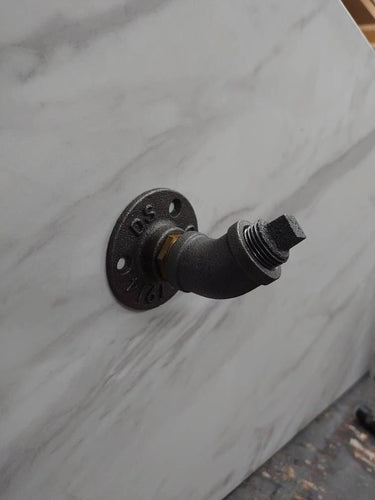 Retro industrial coat hook made from black iron pipe on a white marble wall