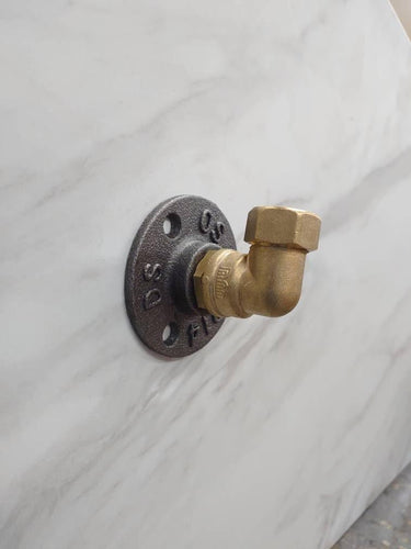 Retro industrial brass coat hook with rustic finish mounted on a white wall