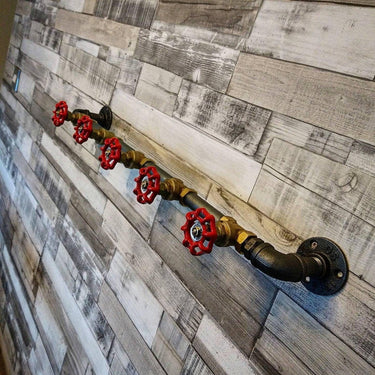 Retro industrial coat rack with red valve hooks mounted on rustic wood panel wall.