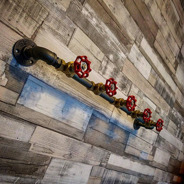 Retro industrial coat hooks made from metal pipe with red valve handles on rustic wood wall.