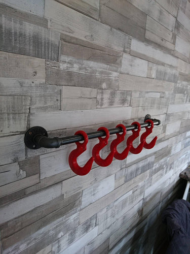Industrial steampunk coat rack with red metal hooks mounted on rustic wood wall