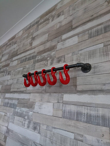 Steampunk industrial coat rack with red hooks on rustic wood panel wall