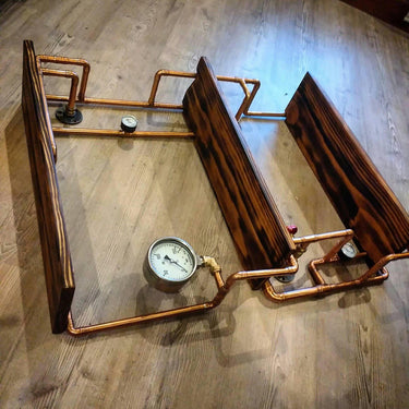 Steampunk industrial hardwood shelves with copper pipe frames and vintage gauges on wood floor