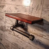 Steampunk pipe toilet paper holder with steel shelf on rustic wood wall.