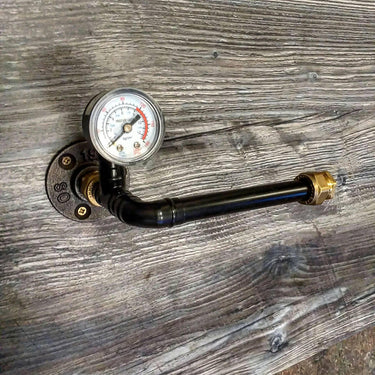 Steampunk pipe toilet paper holder with pressure gauge on rustic wood wall