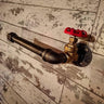 Steampunk industrial pipe toilet paper holder with red valve on rustic wood wall.
