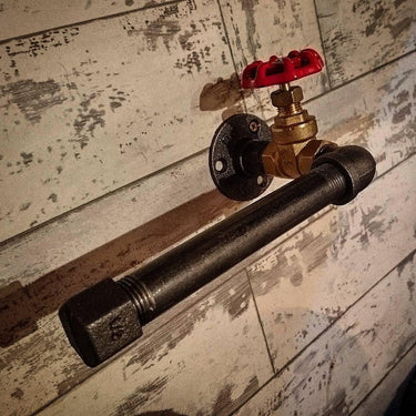 Steampunk industrial pipe toilet paper holder with red valve on rustic wood wall.