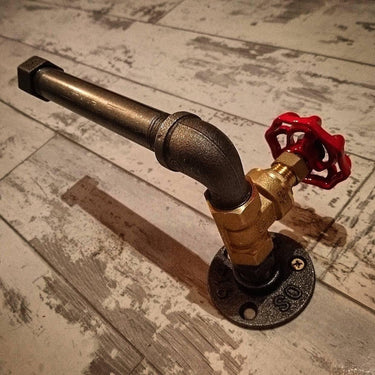 Industrial steampunk pipe toilet paper holder with red valve on rustic wooden floor