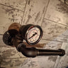 Steampunk pipe toilet paper holder with vintage steel gauge against rustic tiled wall