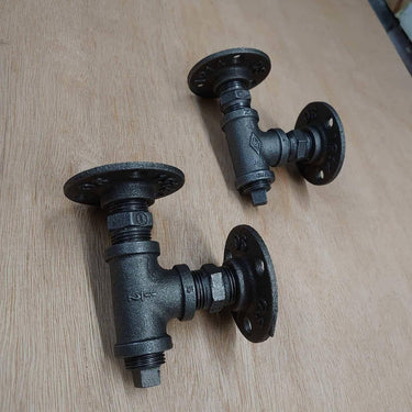 Pair of steampunk pipe wall brackets with industrial black iron fittings on wooden surface