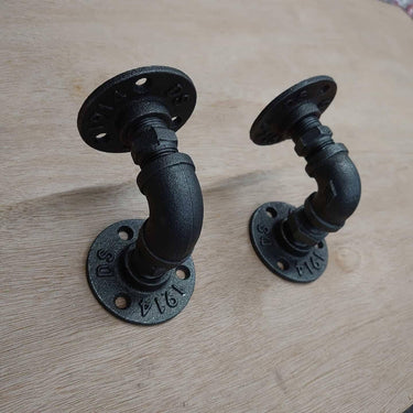 Pair of black steampunk industrial pipe wall brackets on wooden surface