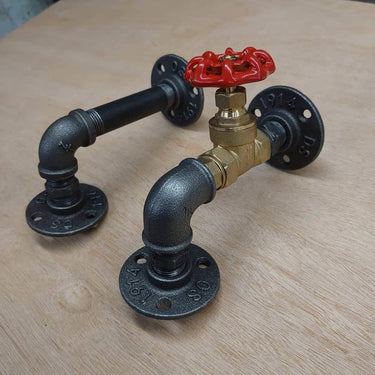 Pair of industrial steampunk pipe wall brackets with metal fittings and red valve handle on wood.