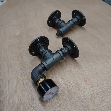 Pair of steampunk pipe wall brackets with flange fittings and a vintage gauge on wooden surface