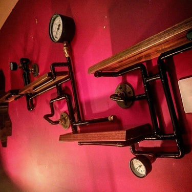 Steampunk industrial pipe shelving unit with wooden shelves and vintage gauges on a red wall
