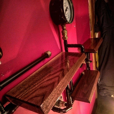 Steampunk industrial shelving unit with wood shelves and metal pipes on a red wall