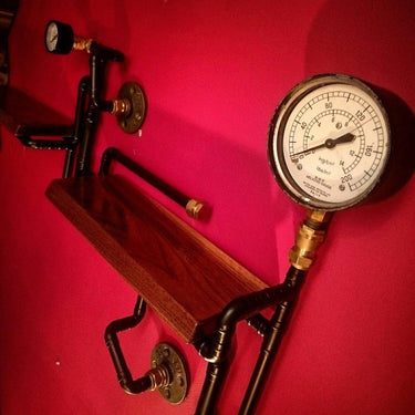 Steampunk shelving unit with industrial pipe design, pressure gauges, and wood shelves on red wall