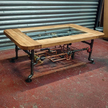Steampunk coffee table with glass top, exposed copper pipes, and industrial metal legs