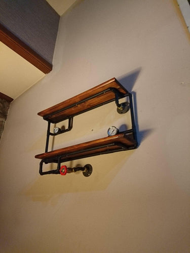 Industrial steampunk shelving unit with wood shelves, iron pipes, pressure gauges, and valve handles mounted on a beige wall.