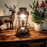 Vintage industrial table lamp with exposed bulb on wooden table, beside plant and deer sculpture