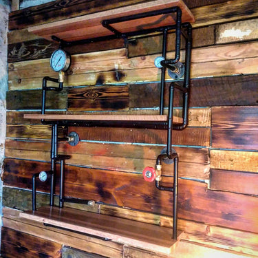 Steampunk shelving unit with wood shelves and black pipe frame, featuring vintage gauges, mounted on a rustic wood wall.