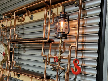 Industrial steampunk shelving unit with copper pipes, vintage lantern, and red metal hook.