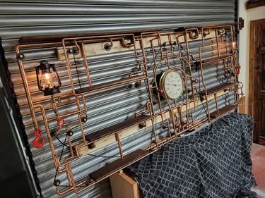Steampunk industrial shelving unit with copper pipes, wood shelves, vintage gauge, and lamps.